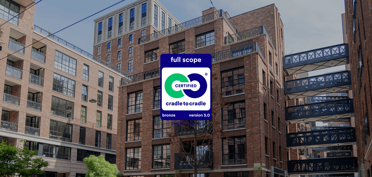 The Cradle to Cradle logo in front of red brick mid-rise buildings.