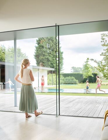 Woman indoors, standing in front of large sliding window.